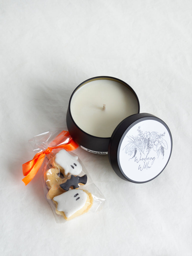 Candle in a tin with Halloween-themed cookies on a white background