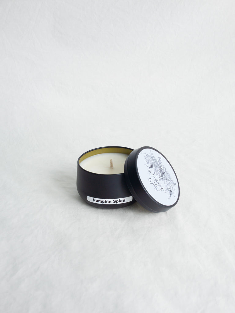 Candle in a black tin labeled 'Pumpkin Spice' on a light gray background