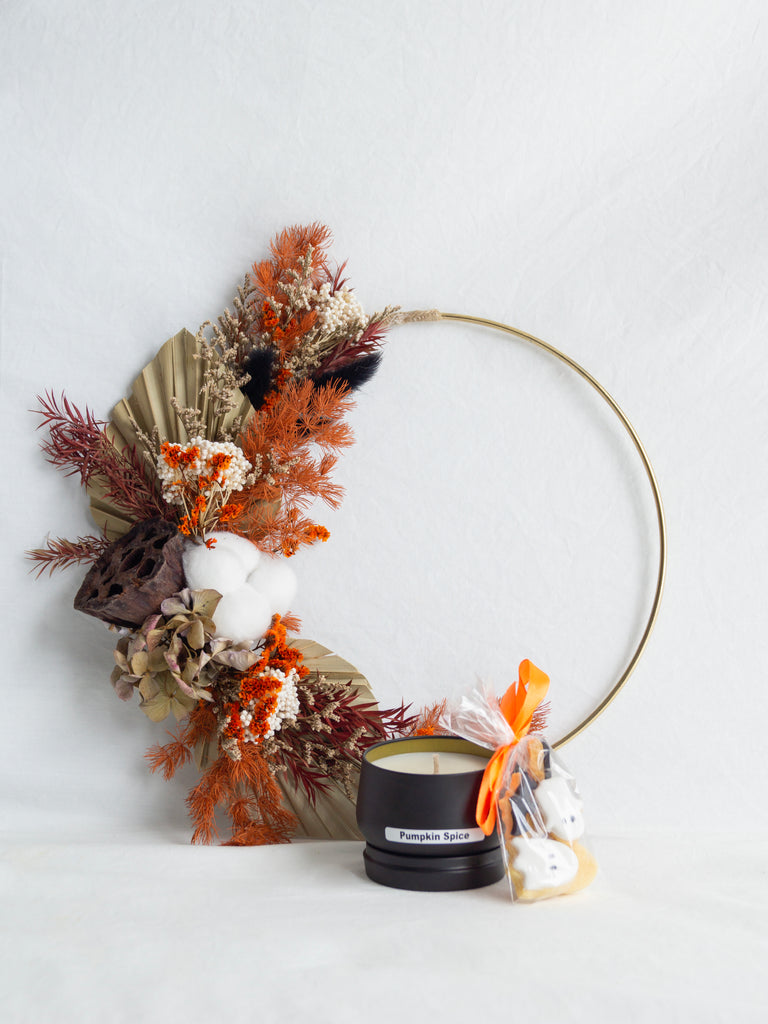 Decorative wreath with dried foliage, a candle, and small gift bag on a white background